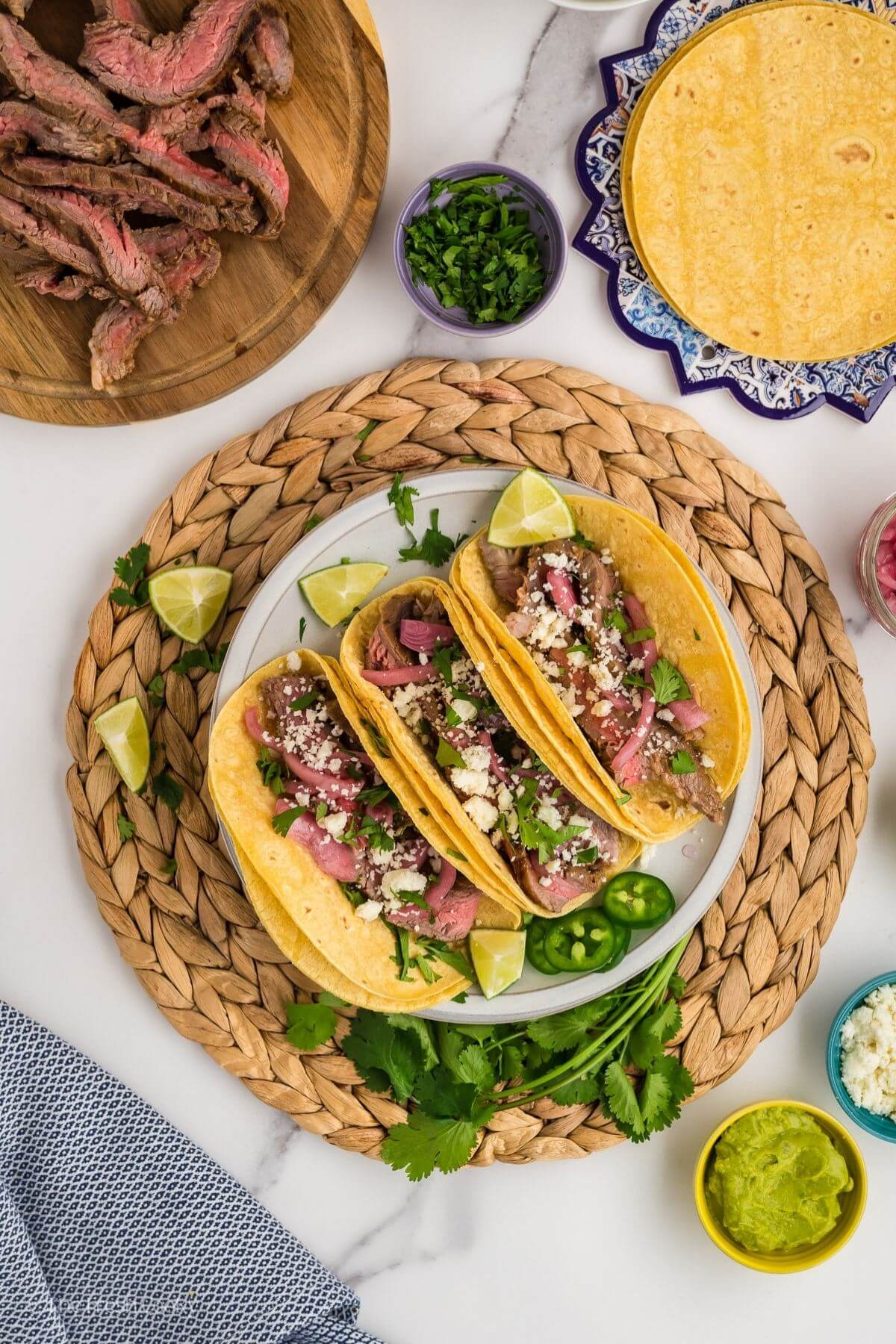 Overhead shot of carne asada tacos on a plate next to more tortillas and meat.