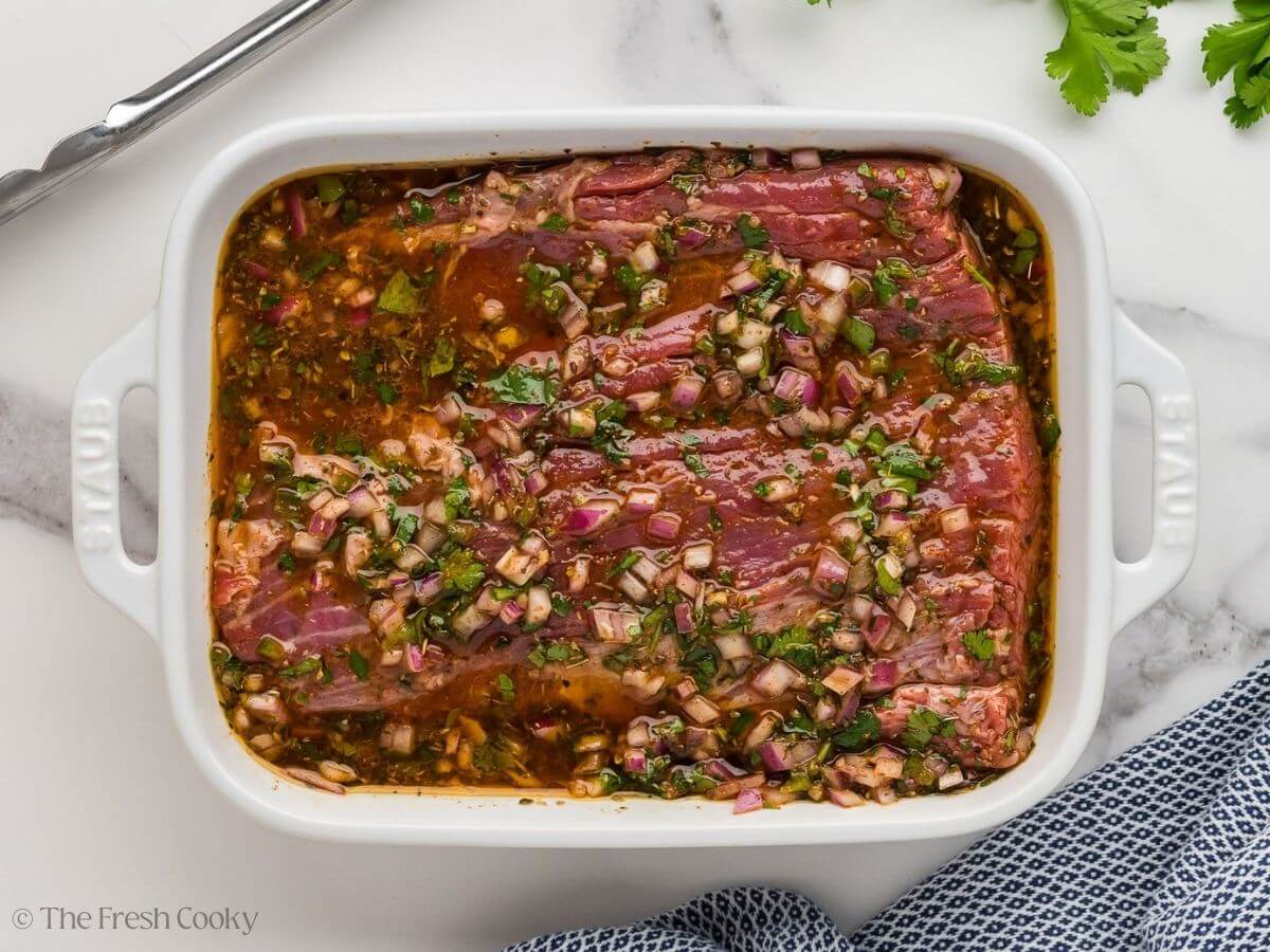 Flank steak added to the marinade in a white baking dish.