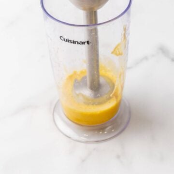 Immersion blender blending egg yolks in a plastic container.