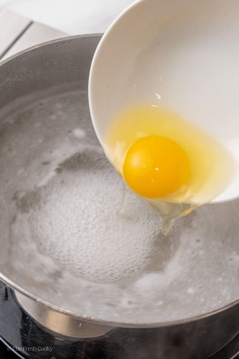 Adding an egg into the boiling water to poach it.