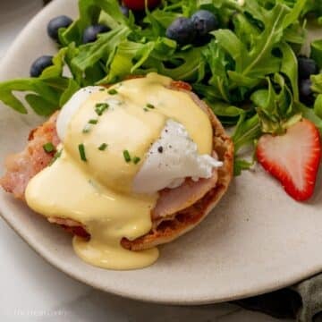 Eggs benedict with creamy hollandaise sauce on a plate served with salad and berries.