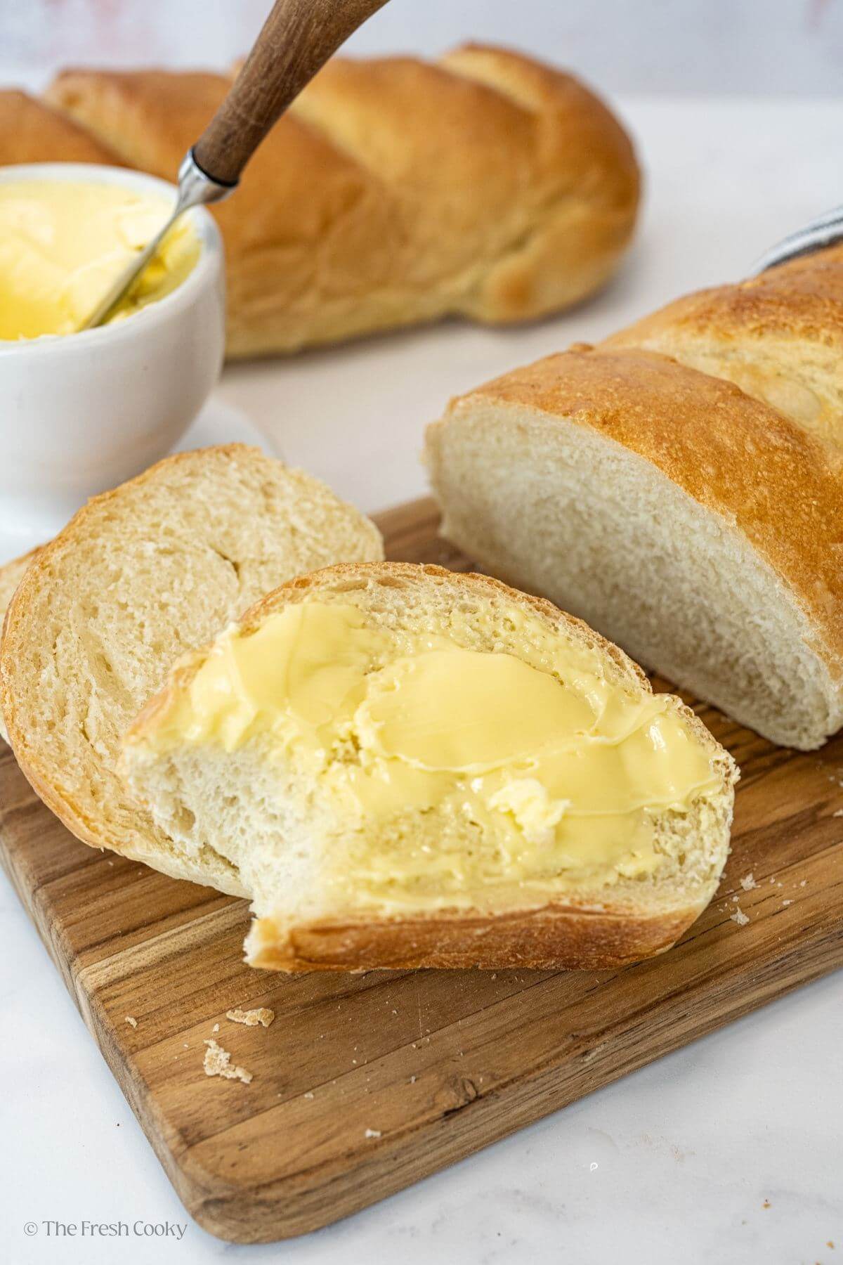 Two slices of French bread with one of them with a slather of butter.