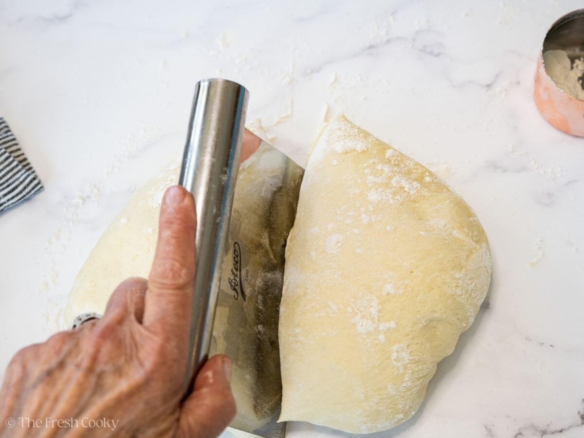 Using a bench scraper to cut the dough into two.