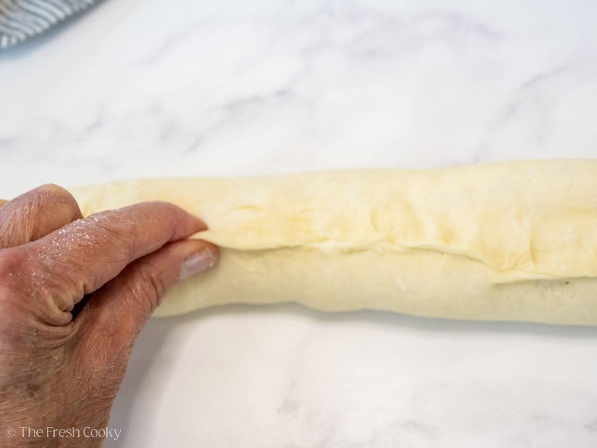 Fingertips sealing the roll of dough together to seal into a log.