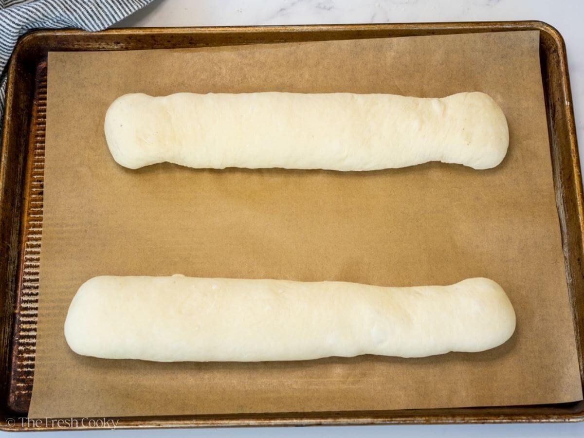 Two French bread dough logs placed on a sheet pan lined with parchment.