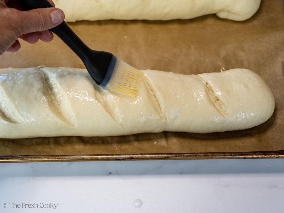 Hand brushing the egg wash on top of the French bread dough.