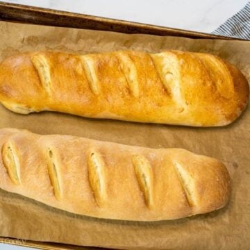 Two loaves of French bread after being baked and still on the sheet pan.