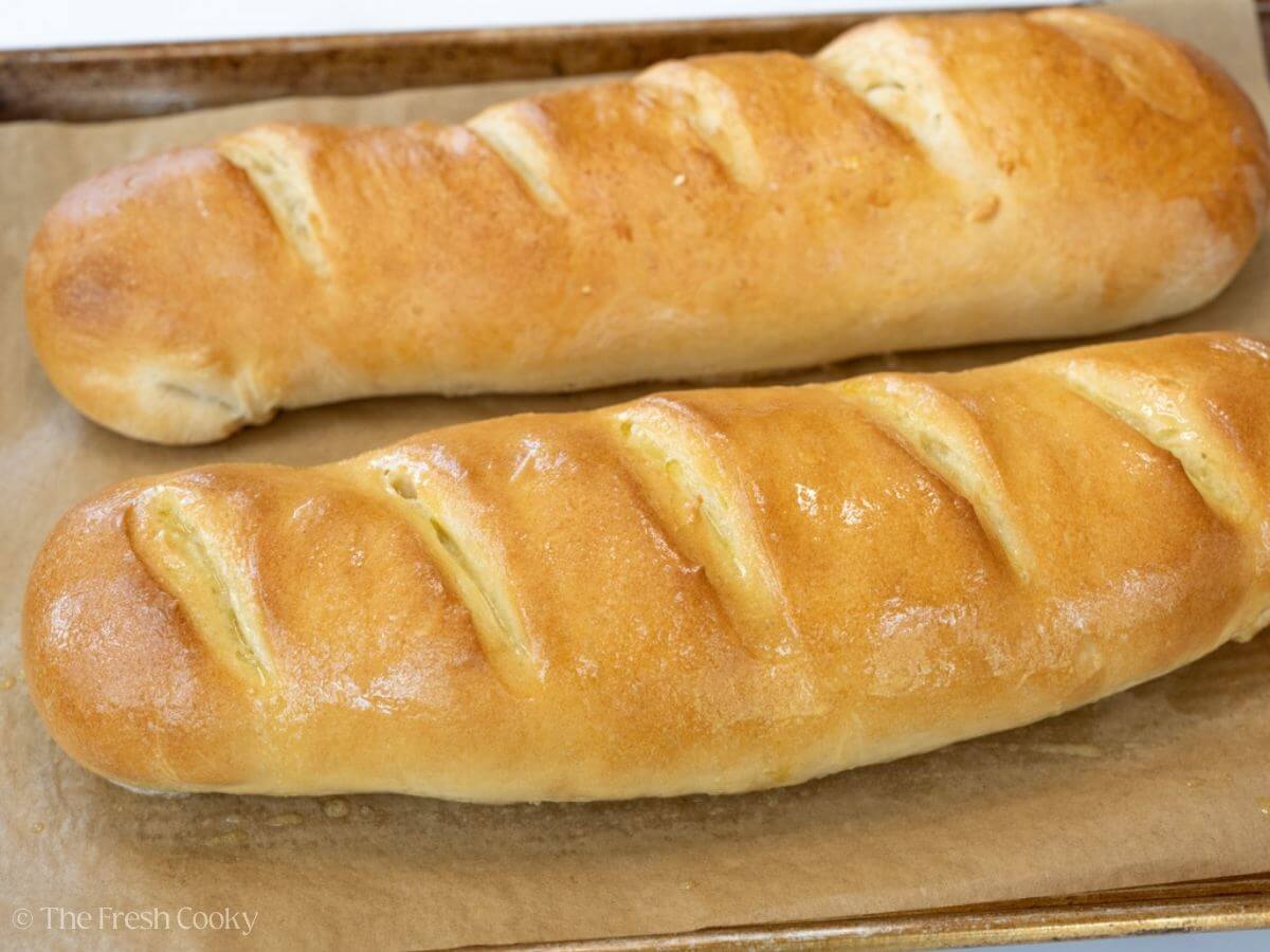 Side view of two French bread loaves on a sheet pan after baking.