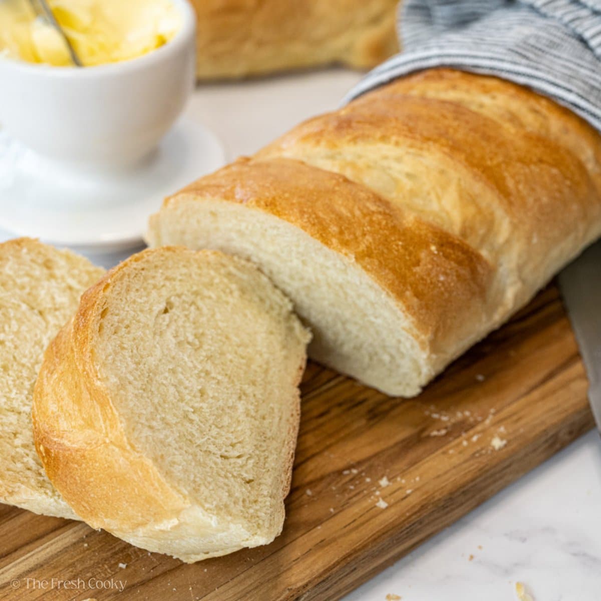 French bread sliced on a cutting board with butter behind.