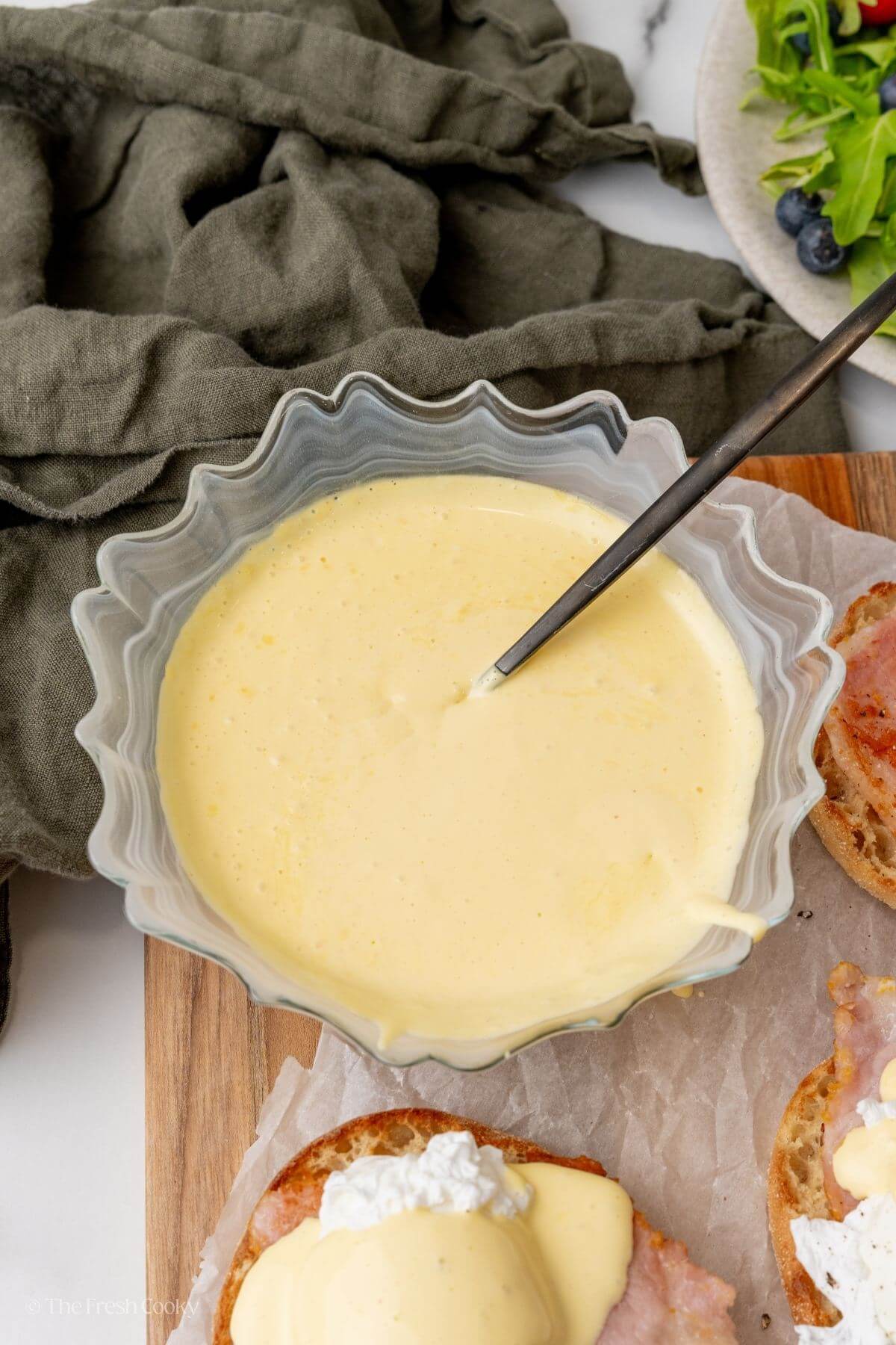Blender hollandaise sauce in a glass serving bowl with a ladle.