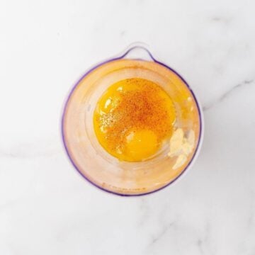 Overhead shot of egg, Dijon, and cayenne pepper in a plastic container.
