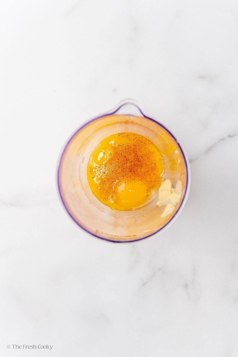 Overhead shot of egg, Dijon, and cayenne pepper in a plastic container.