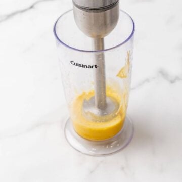 Using an immersion blender to blend the ingredients in a plastic container.