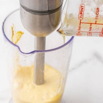 Pouring the butter into the hollandaise sauce in a container with an immersion blender.