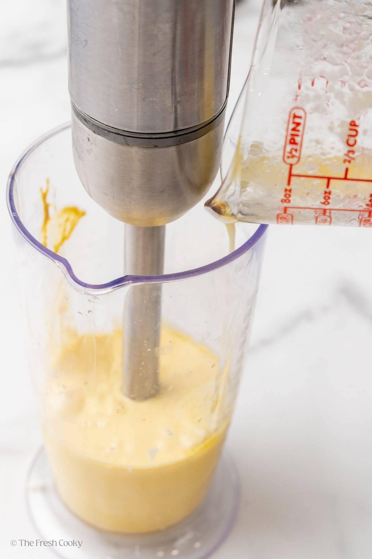Pouring the butter into the hollandaise sauce in a container with an immersion blender.