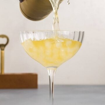 Pouring the skinny margarita from the cocktail shaker into a coup glass with nugget ice.