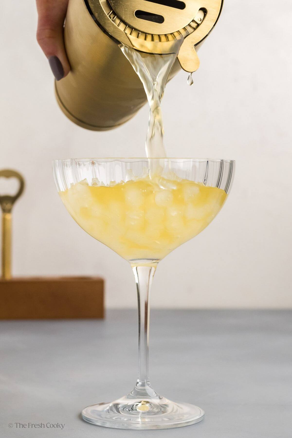 Pouring the skinny margarita from the cocktail shaker into a coup glass with nugget ice.
