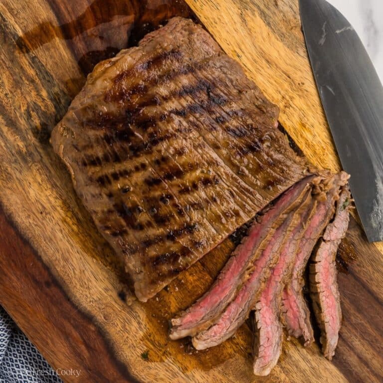 A slab of carne asada grilled and sliced on a cutting board.