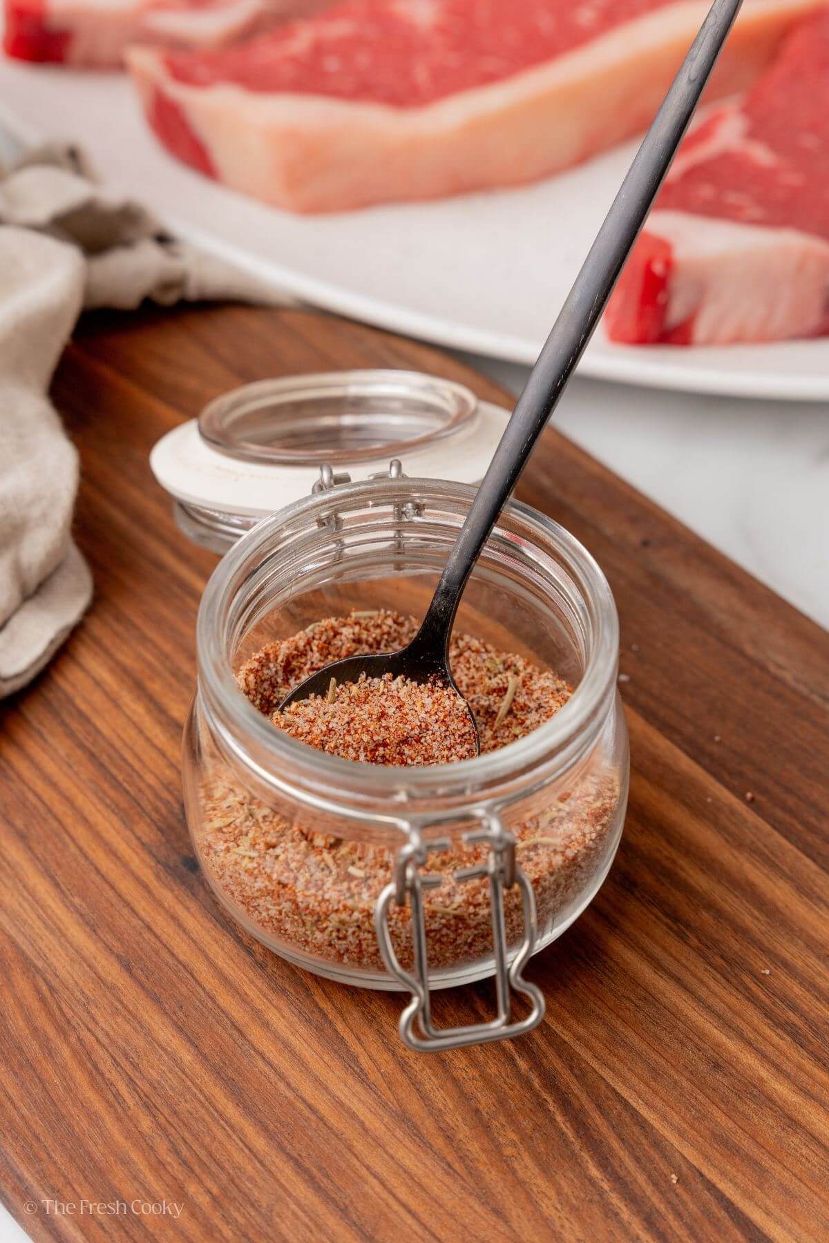 Spoon in a jar of steak seasoning on a wooden board.