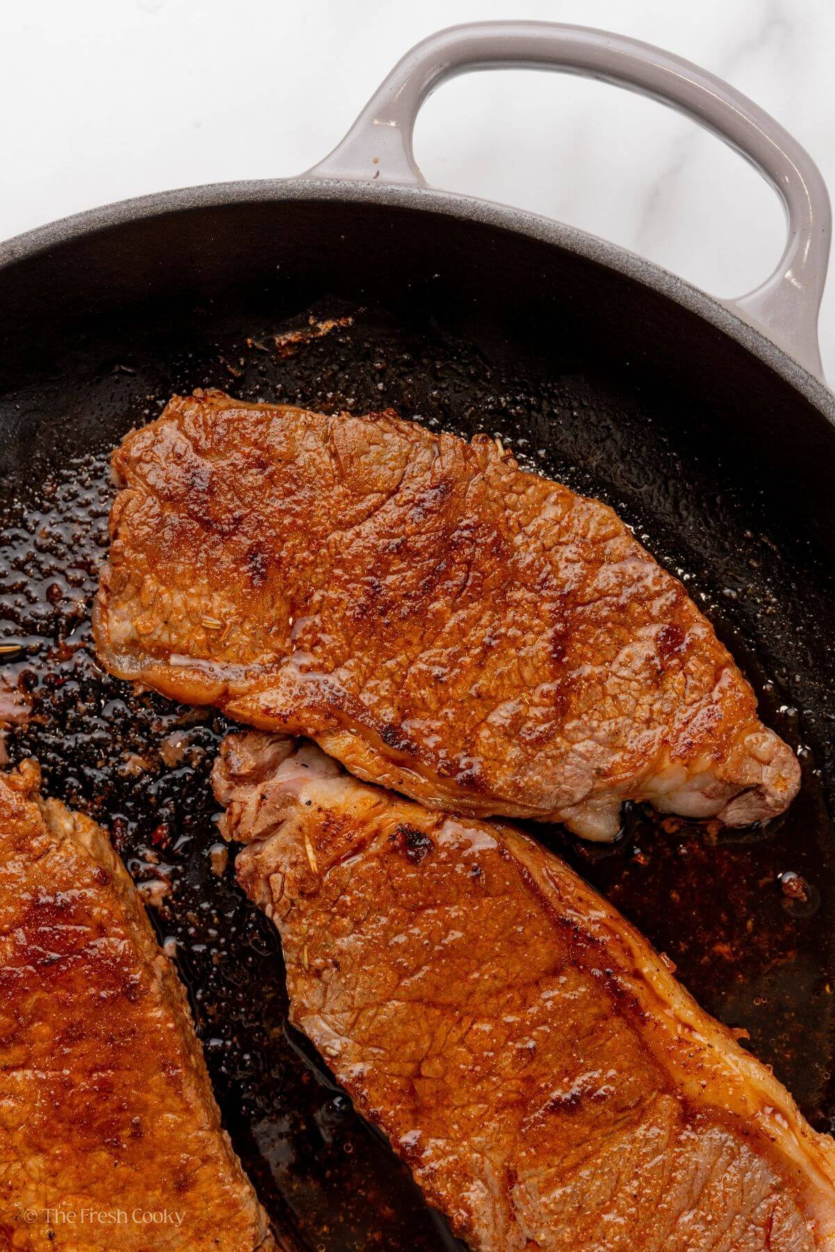 Steak seasoned with homemade steak seasoning cooking in a skillet.