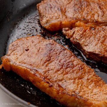 Steak seasoning on steak searing in a cast iron skillet.