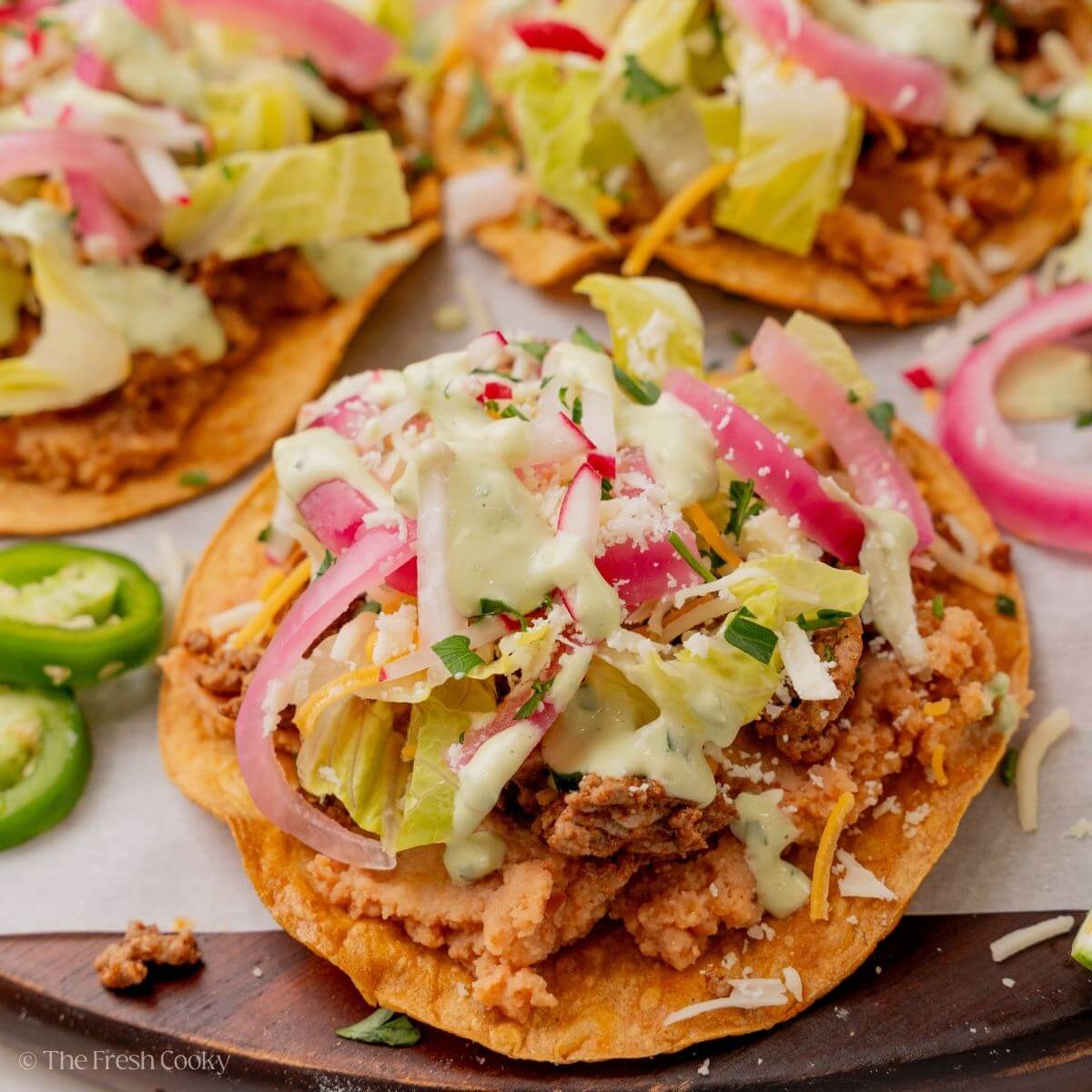 Tostadas served on a wooden board with various toppings on top.