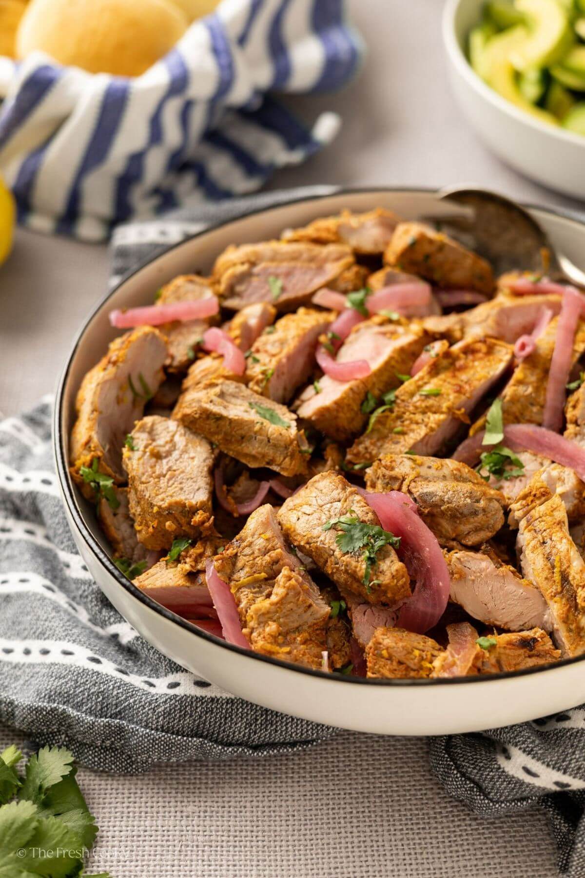 Side view of sliced achiote pork tenderloin with pickled onions in a bowl.