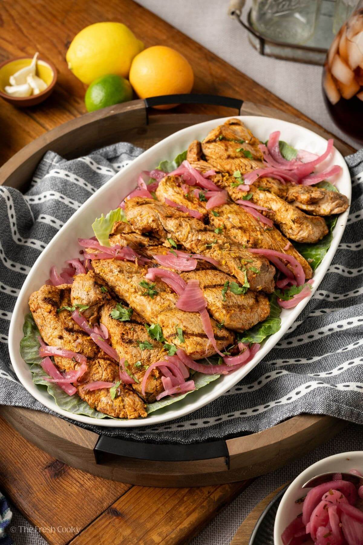 Pork tenderloin served on a white serving platter with pickled onions on top.