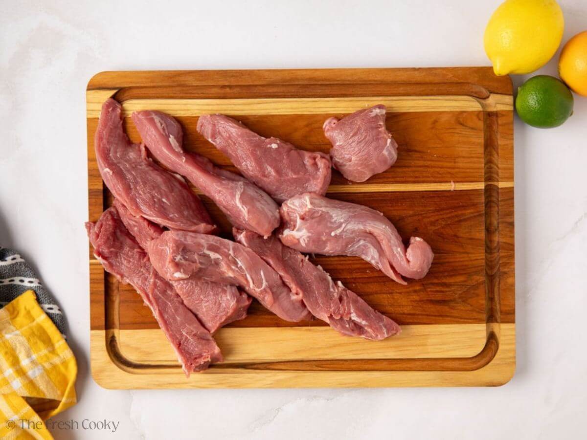 Sliced pork tenderloin on a wooden board.
