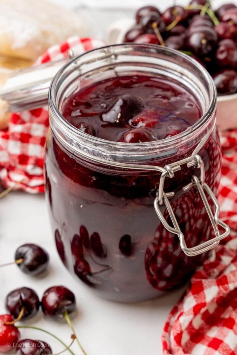 Cherry pie filling in a jar with fresh cherries in the background.