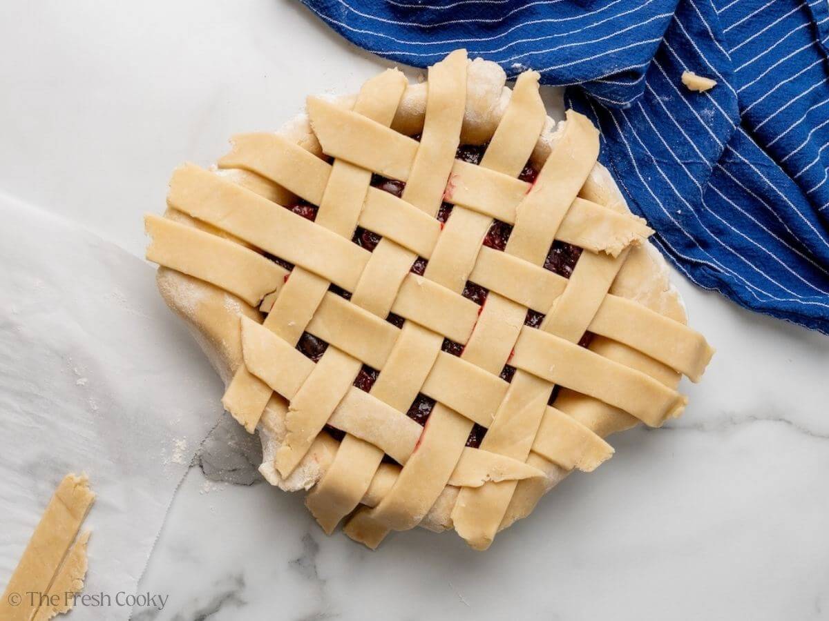 Pie dough in a lattice pattern on top of the pie before trimming the edges.