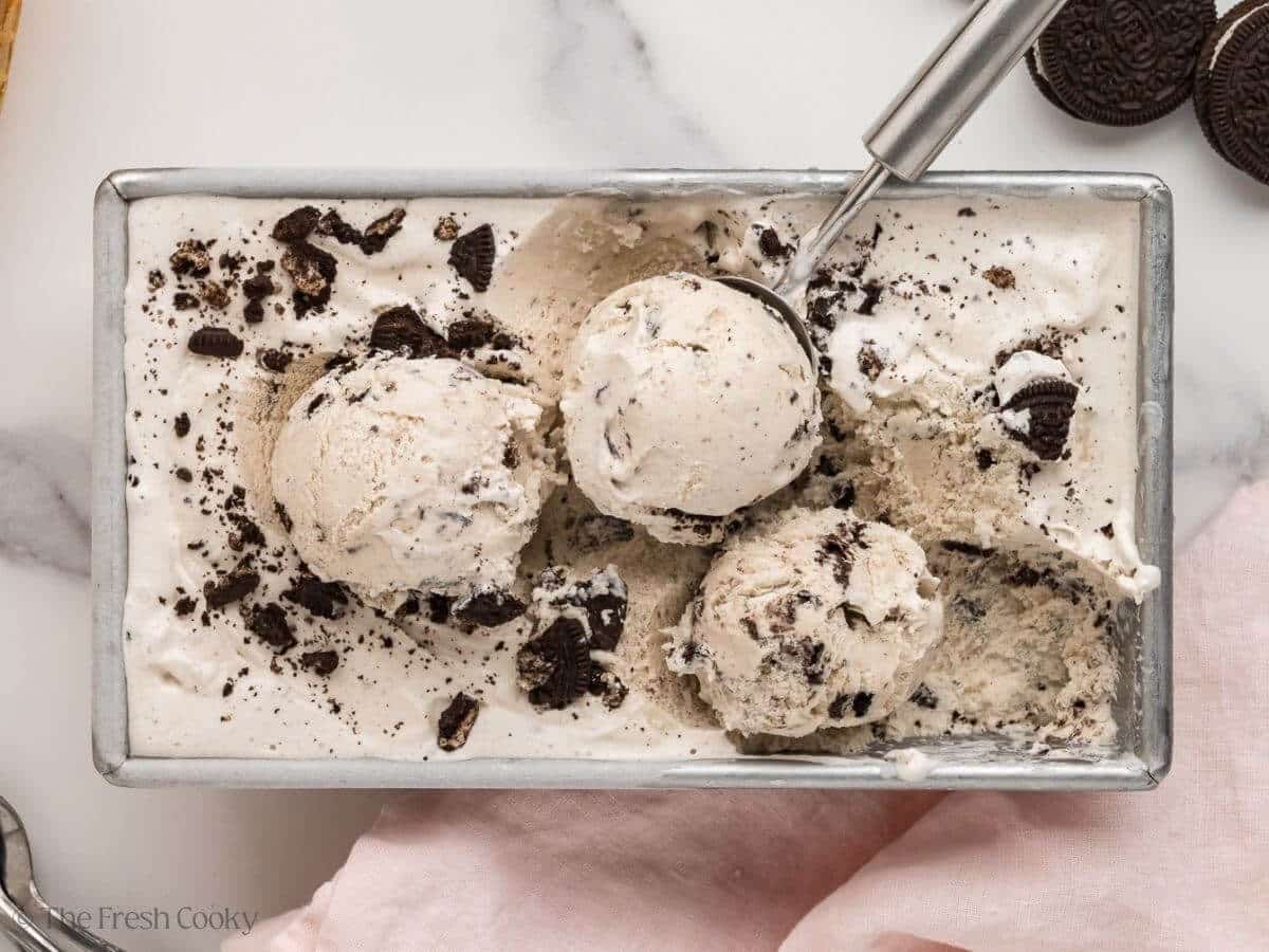 Overhead shot of cookies and cream ice cream in a loaf pan with an ice cream scoop.