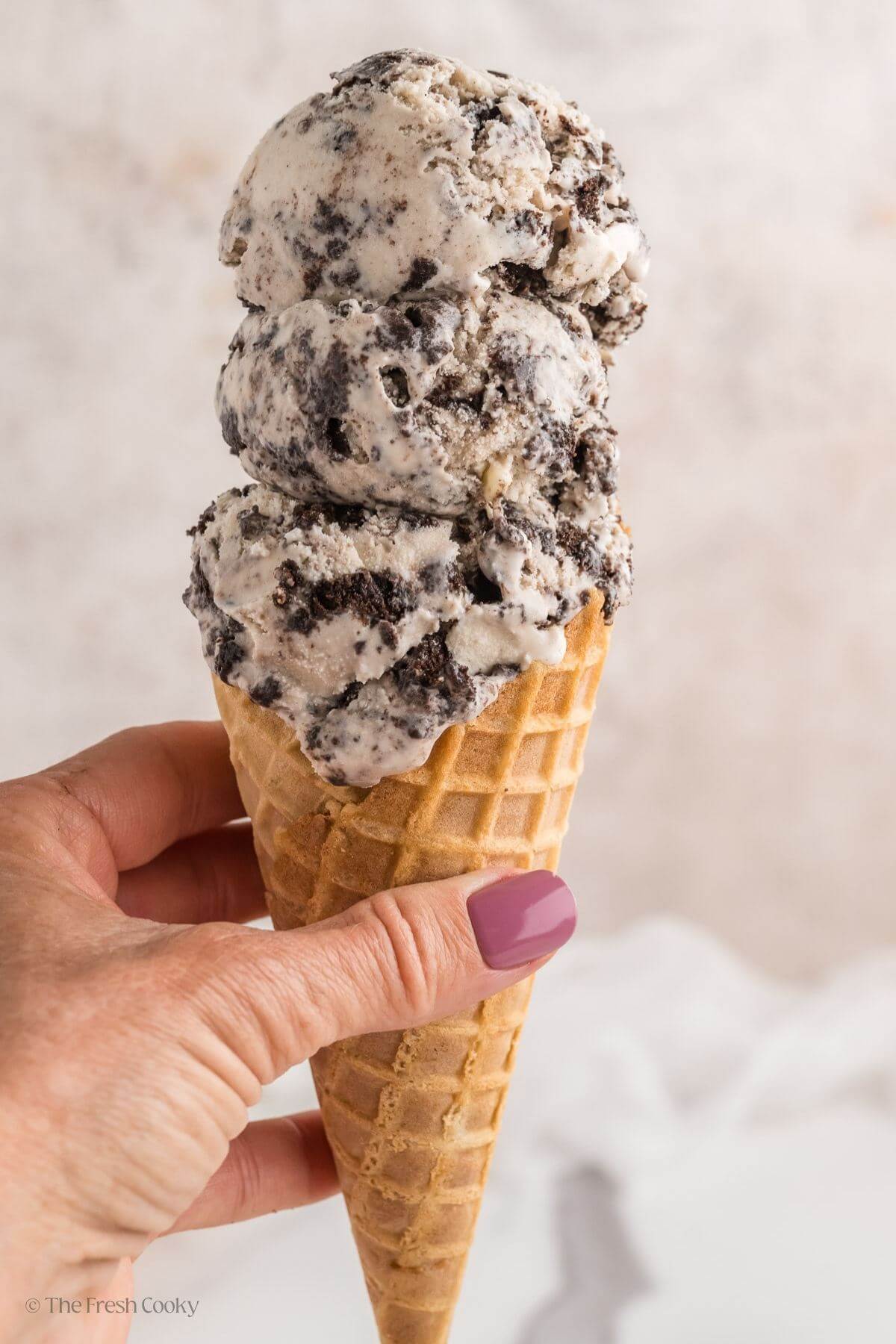 Hand holding an ice cream cone with three scoops of cookies and cream ice cream.