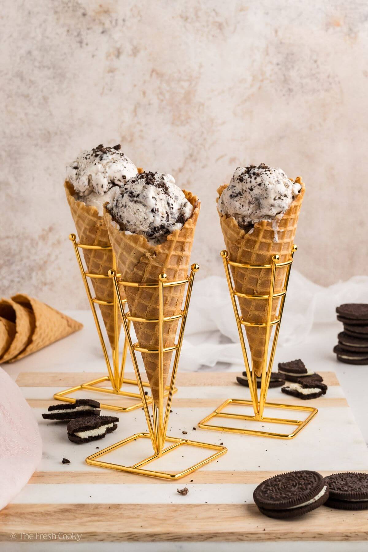 Three cones of cookies and cream ice cream with scattered Oreos around.