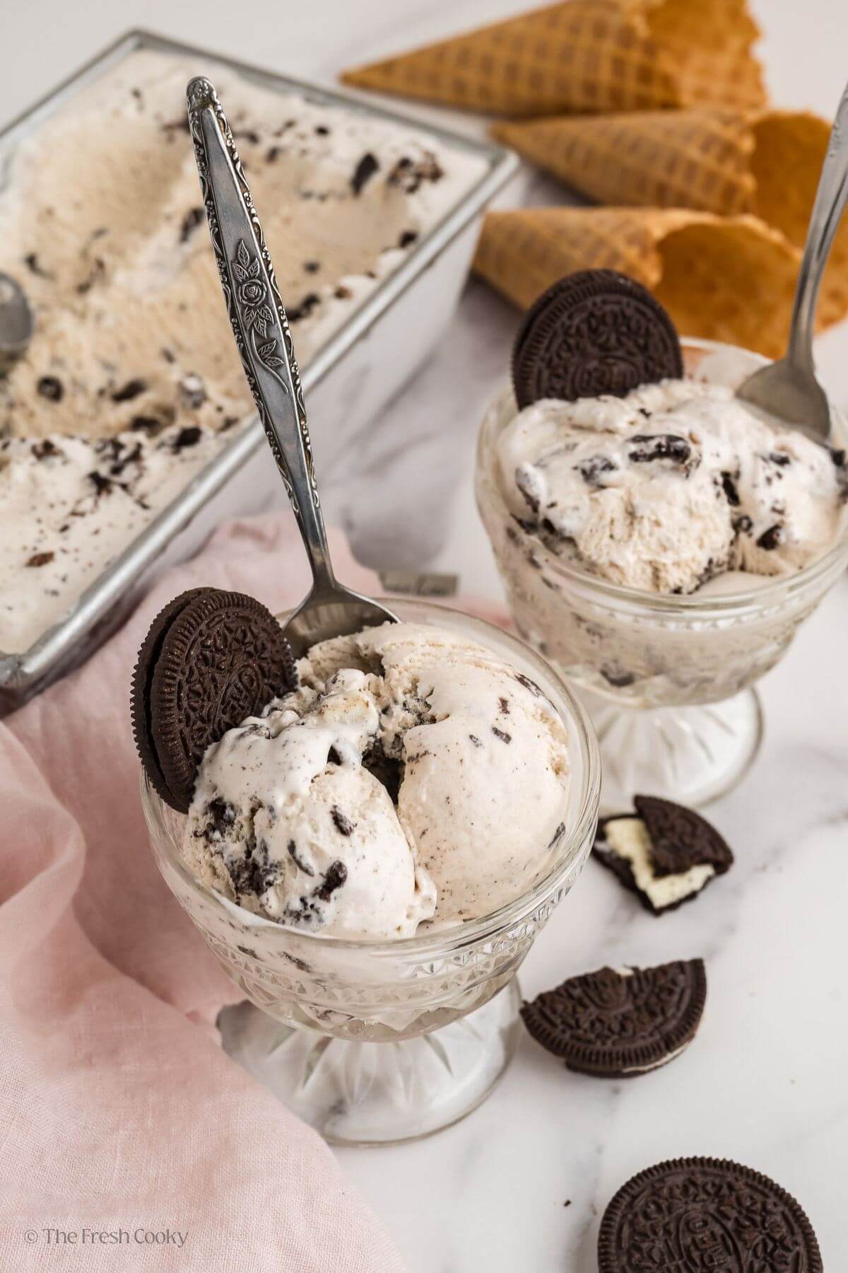 Two cups of cookies and cream ice cream with spoons, garnished with oreos.