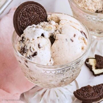 A pretty glass bowl filled with scoops of cookies and cream ice cream with an Oreo stuck on top.