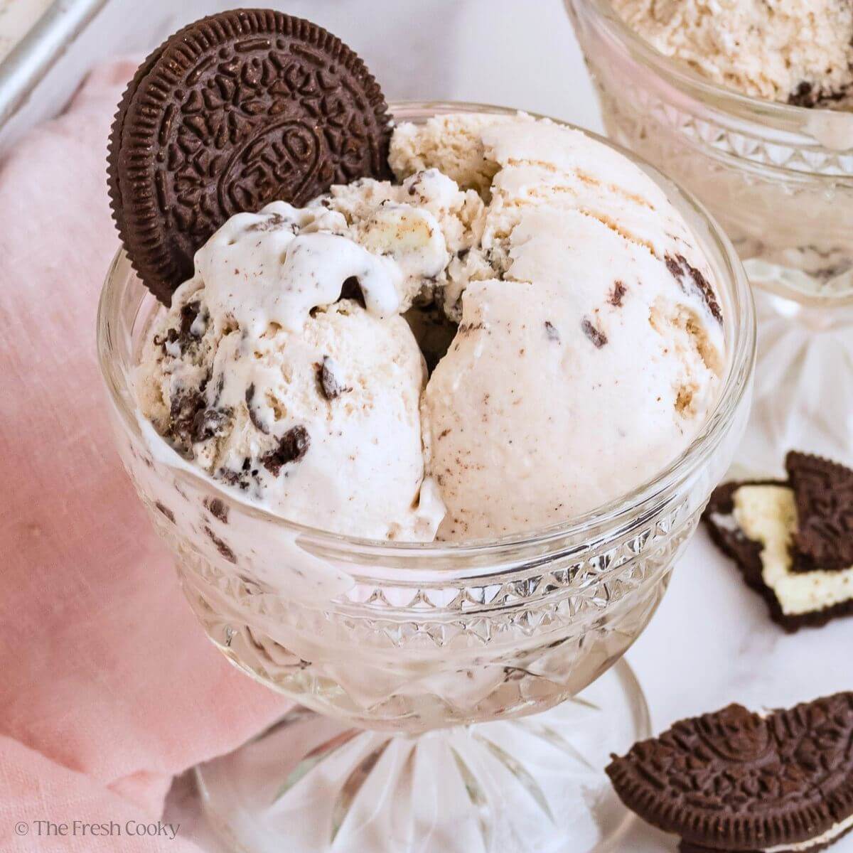 A pretty glass bowl filled with scoops of cookies and cream ice cream with an Oreo stuck on top.