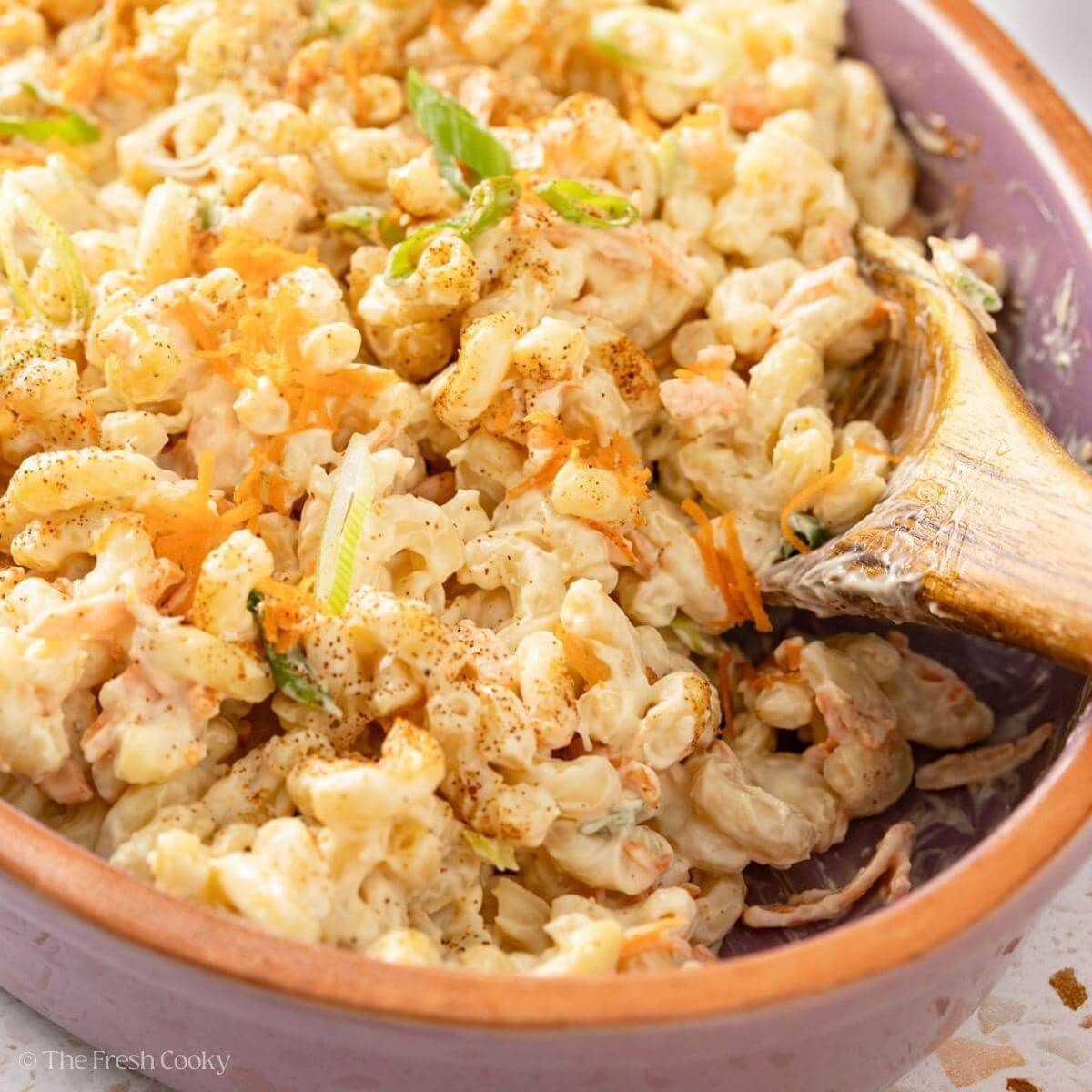 Sideview of Hawaiian macaroni salad in a clay bowl with a wooden spoon.