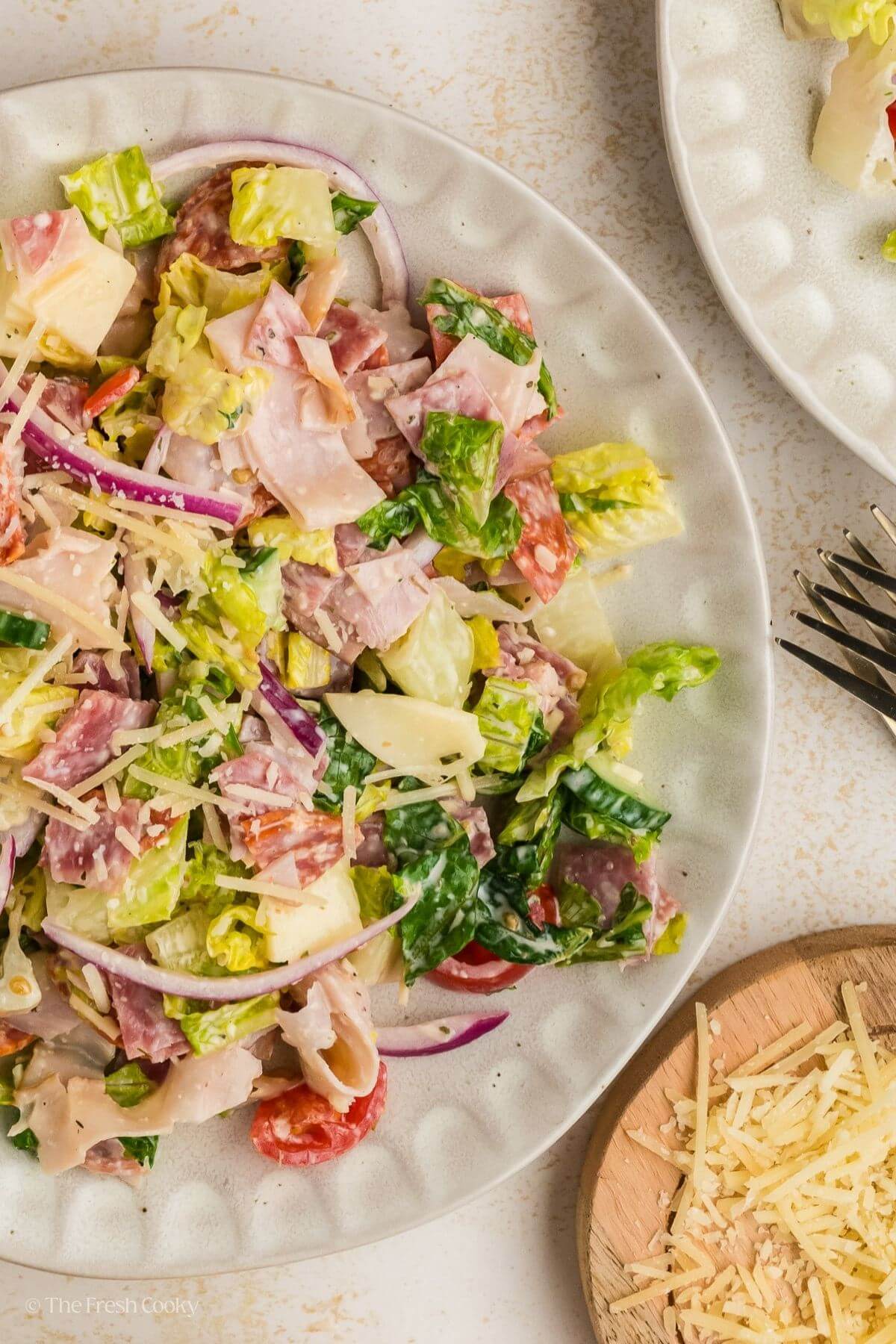 Overhead shot of Italian grinder salad on a white plate next to shredded parmesan.