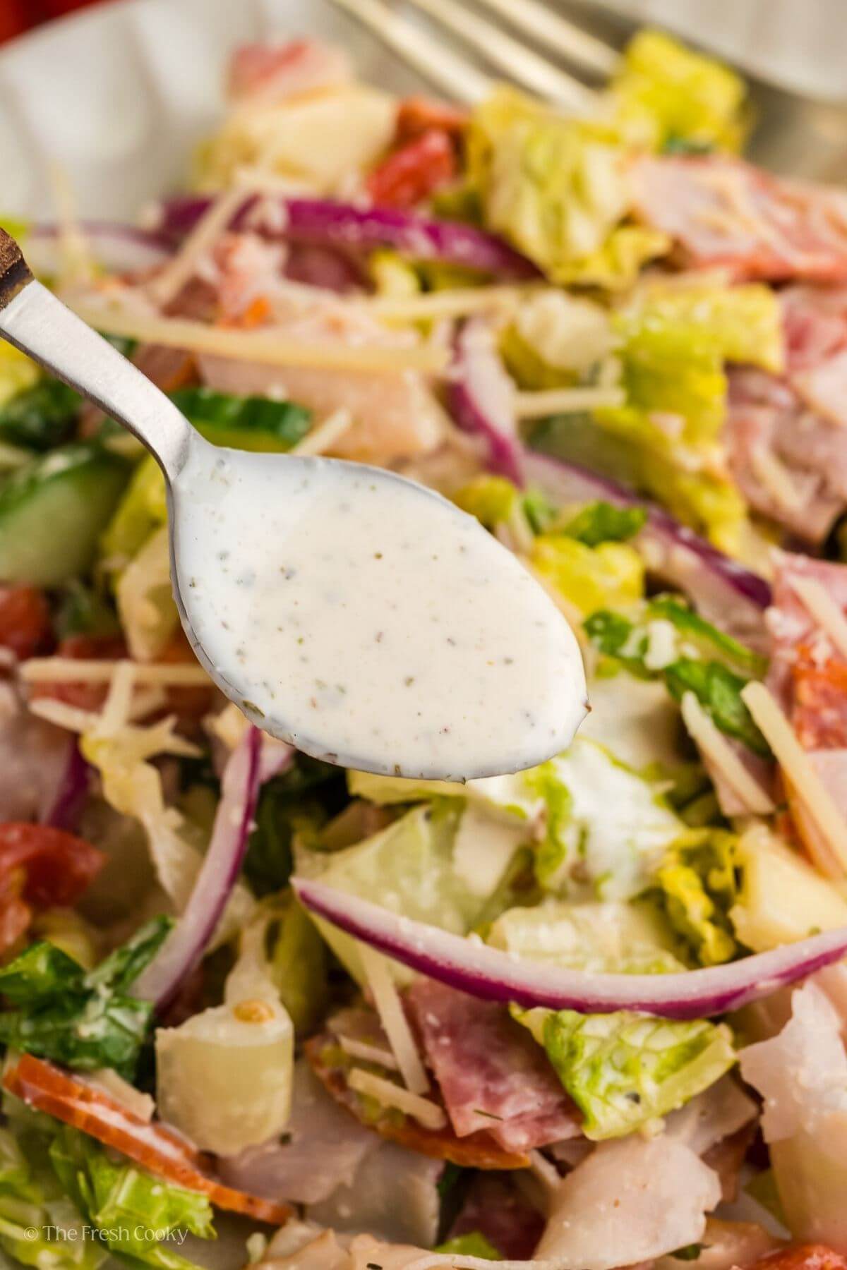 Using a spoon to drizzle dressing on top of the salad on a plate.
