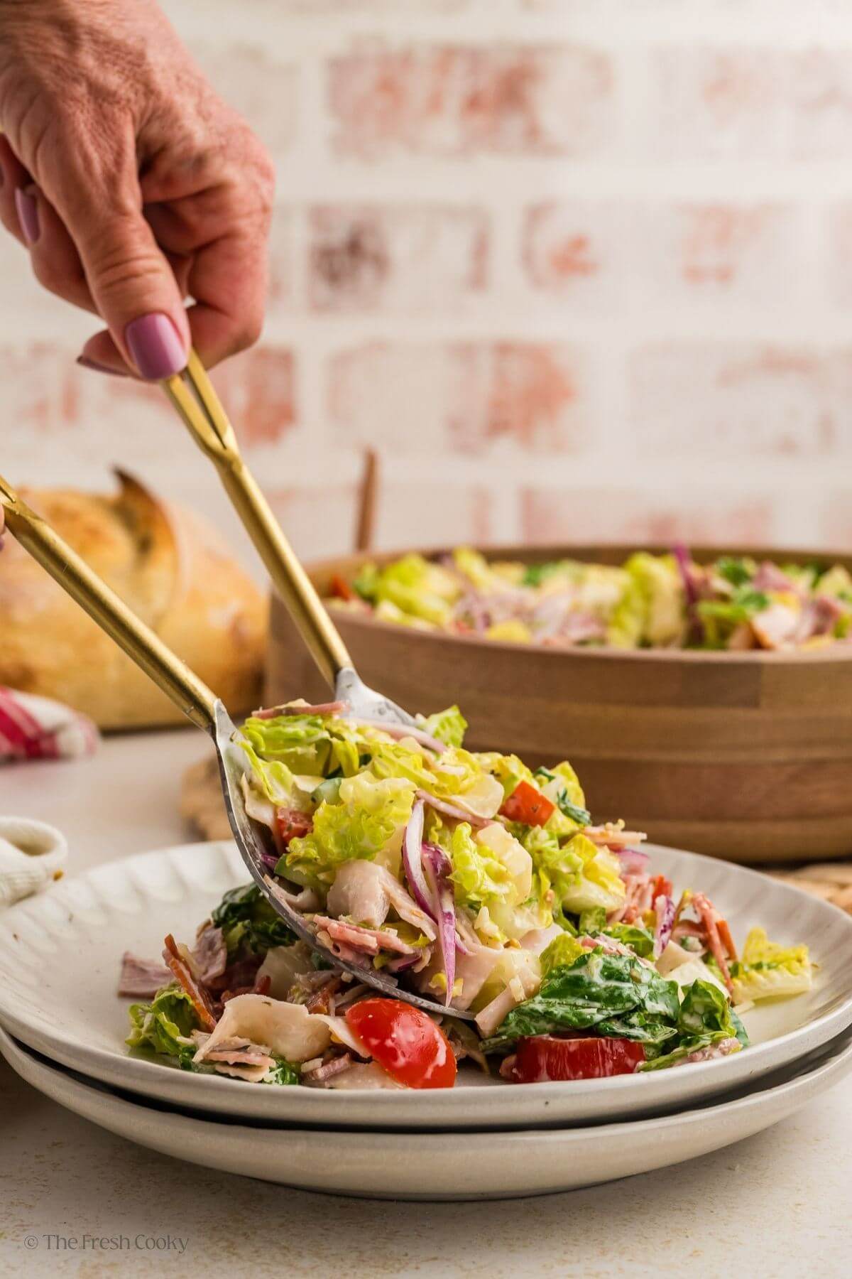 Hands using salad tongs to serve grinder sub salad on a plate.