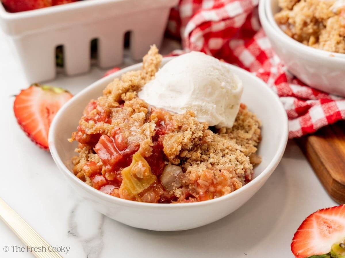Strawberry rhubarb crisp in a bowl with a scoop of ice cream on top.