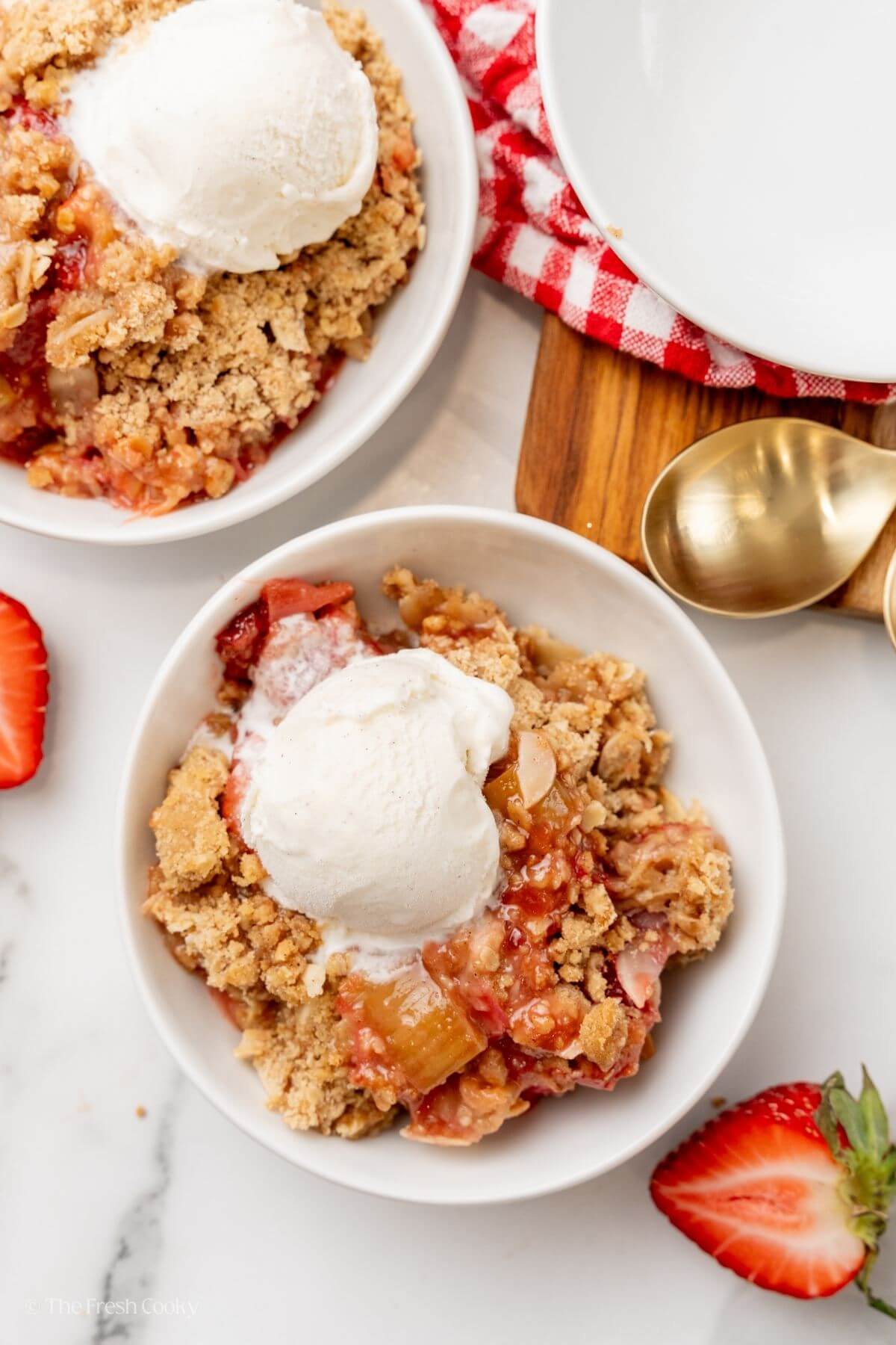 Overhead shot of two bowls of strawberry rhubarb crisp each served with a scoop of ice cream.