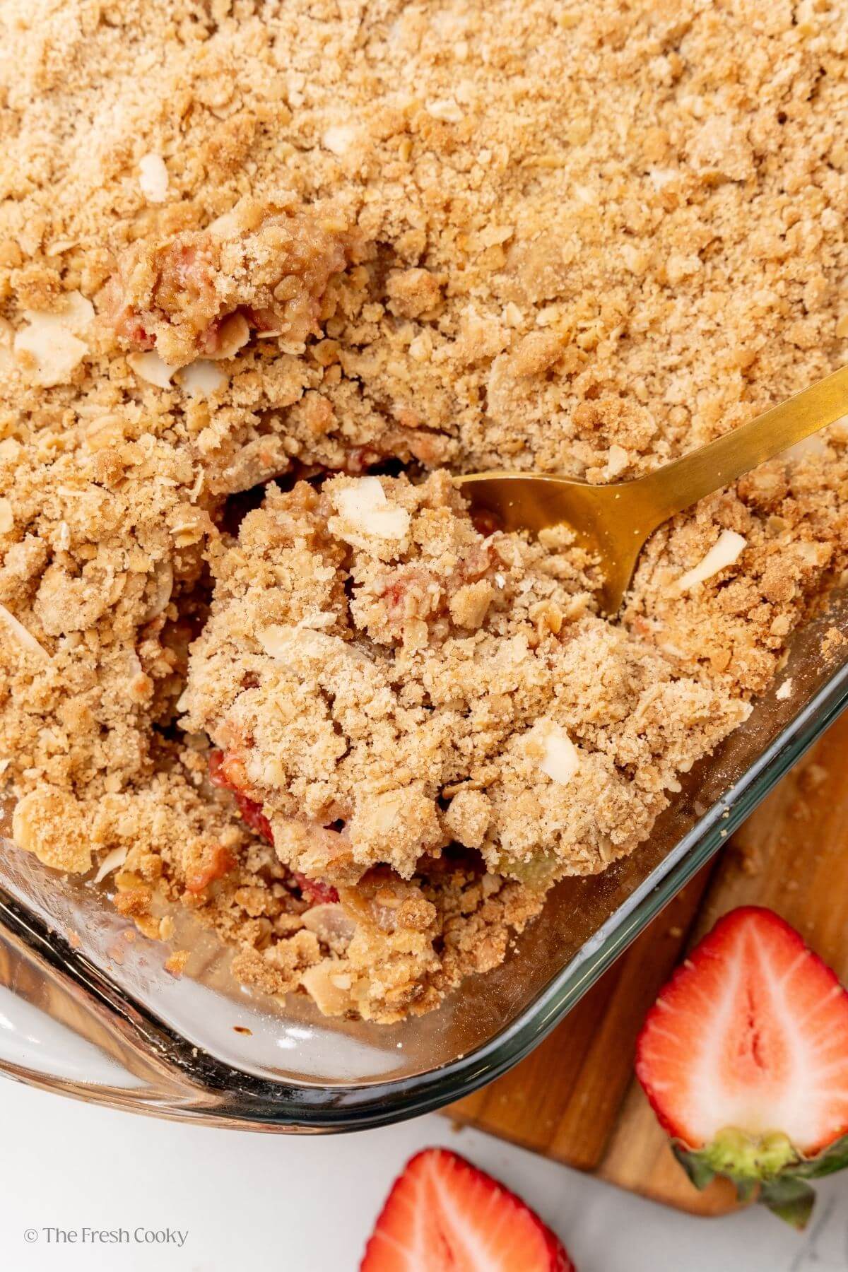 Baking dish of strawberry rhubarb crisp with a spoon digging in.