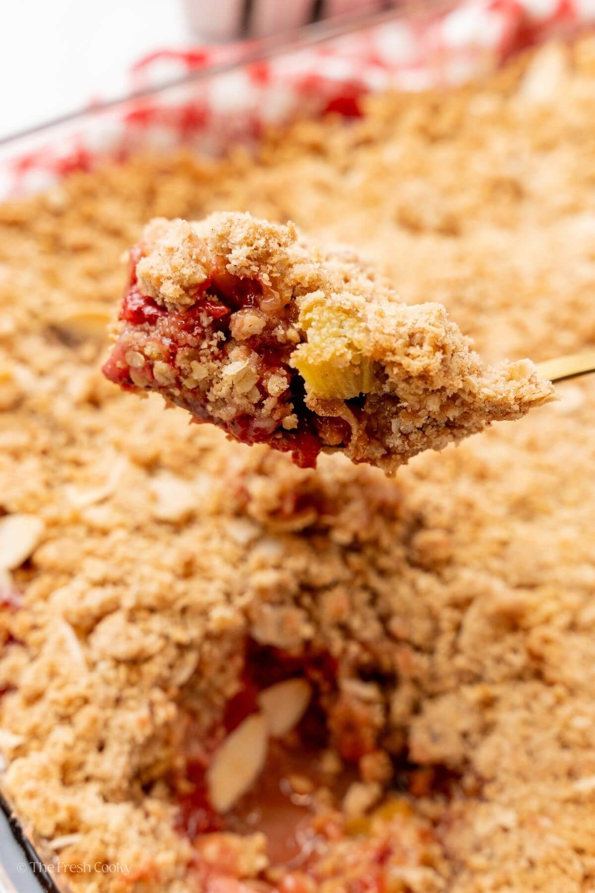 Spoon with rhubarb strawberry crisp on it with the rest of the crisp underneath it.