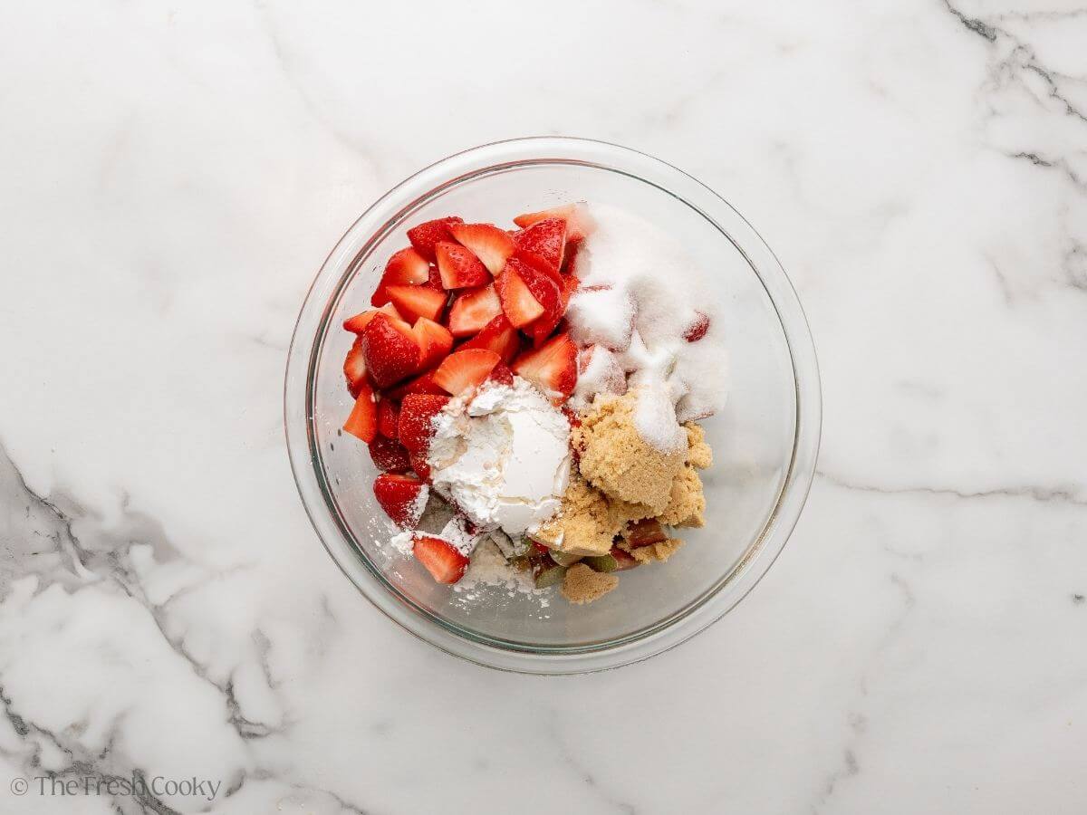 Strawberries and rhubarb in a bowl with sugars and cornstarch.