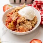 Strawberry rhubarb crisp served in a white bowl with ice cream on top.