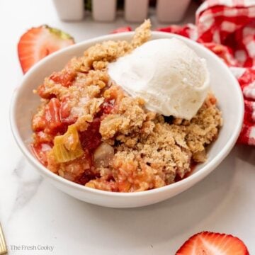 Strawberry rhubarb crisp served in a white bowl with ice cream on top.