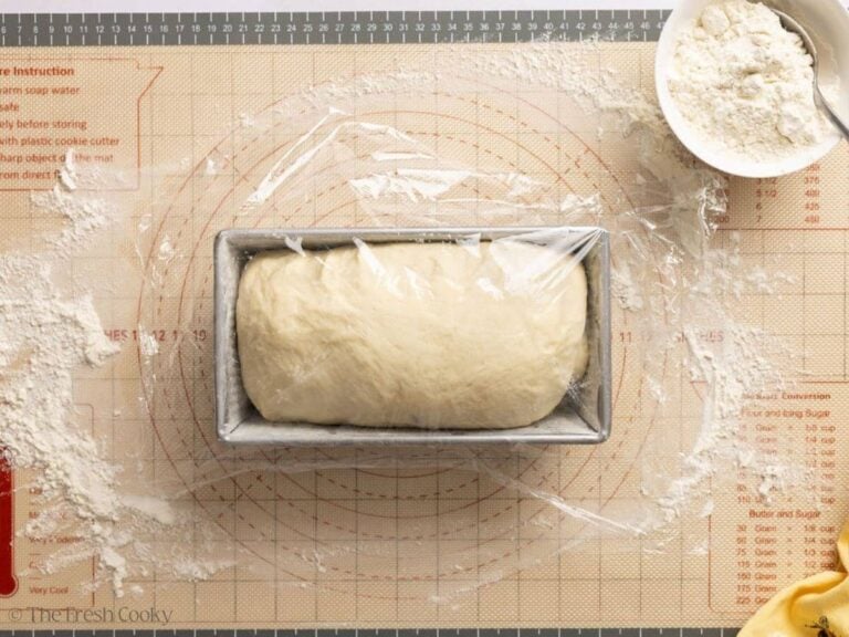 White sandwich bread dough risen in the loaf pan and covered with a piece of plastic wrap.