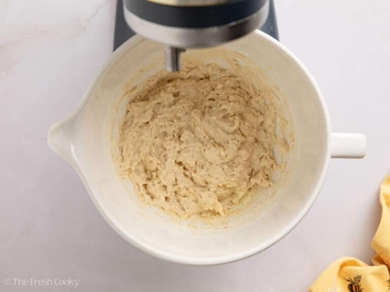 White sandwich dough in the beginning phases in a white mixing bowl of a stand mixer.